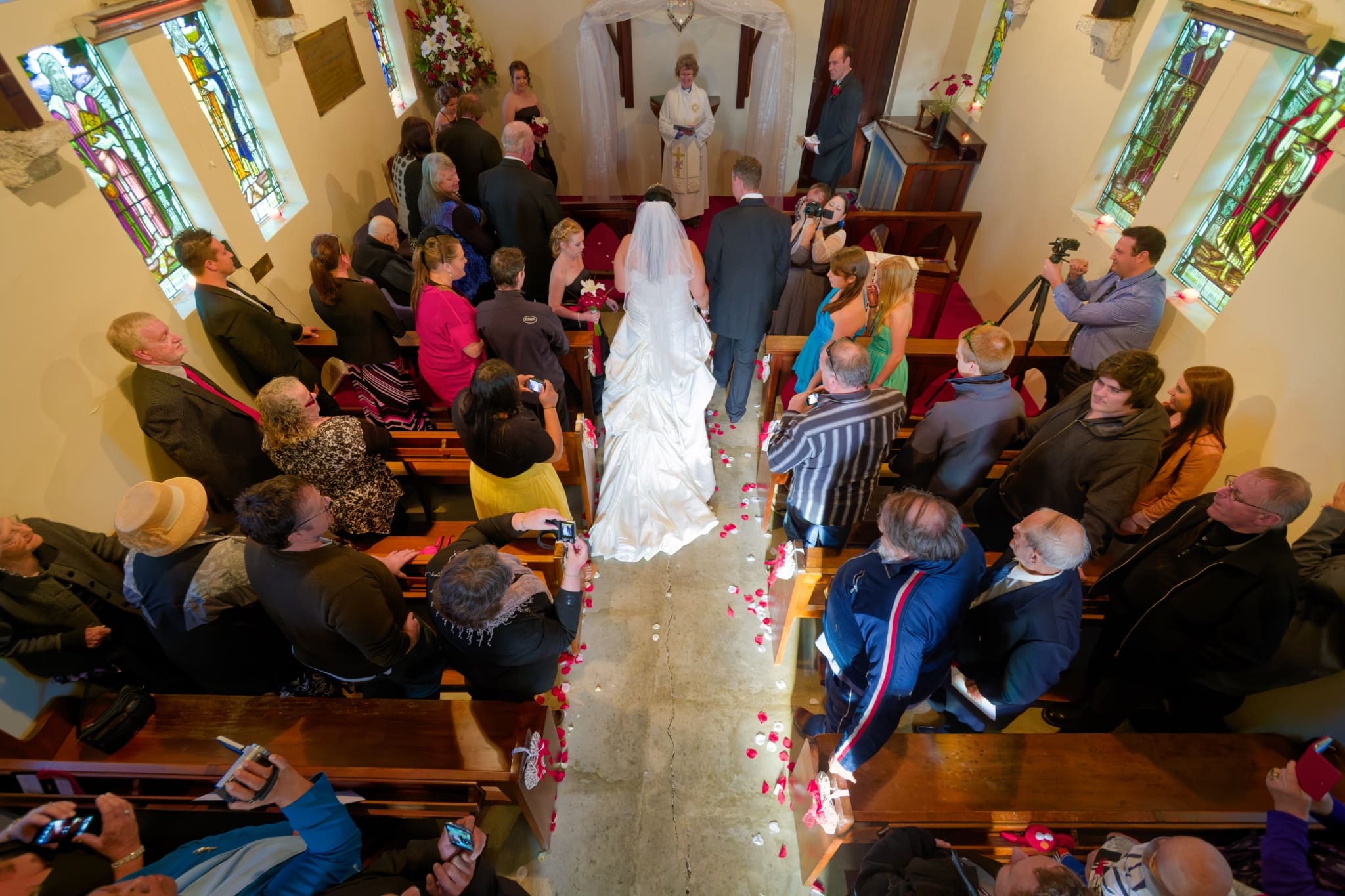 Bride walking down aisle at Saint Oswald's Memorial Church heritage wedding venue ceremony with guests seated in wooden pews and stained glass windows