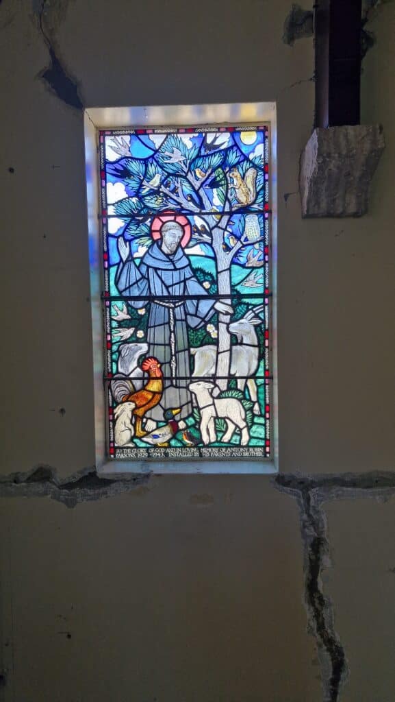 Vibrant stained glass window in historic Saint Oswald's Memorial Church featuring Saint Francis with animals, blue sky and tree, illuminated by natural light in this heritage wedding chapel venue.