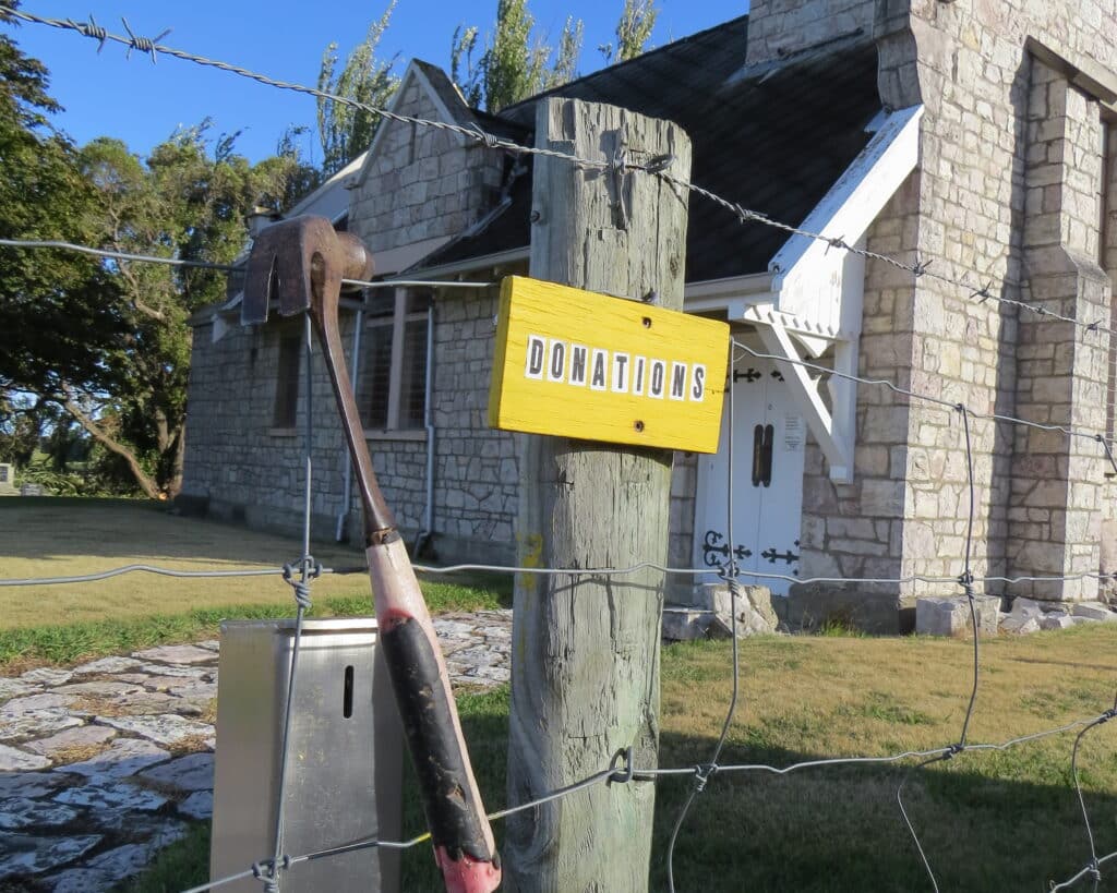 Historic stone chapel with donations sign and weathered wooden pole, ideal charming heritage wedding venue backdrop