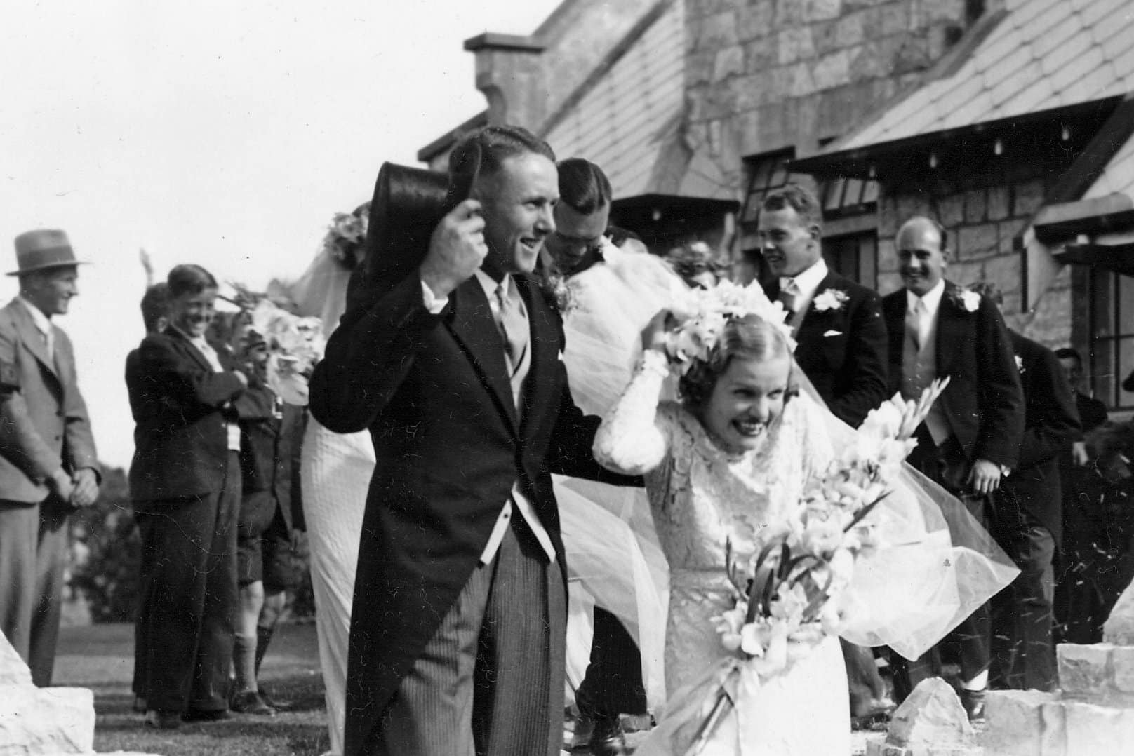 Historic wedding ceremony outside heritage stone church with bride, groom, and guests in vintage attire enjoying joyful celebration at traditional chapel venue.